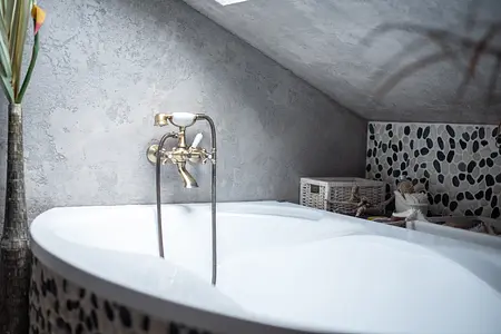 Wnętrze łazienki z białą wanną i szarymi ścianami w stylu rustykalnym i industrialnym.
