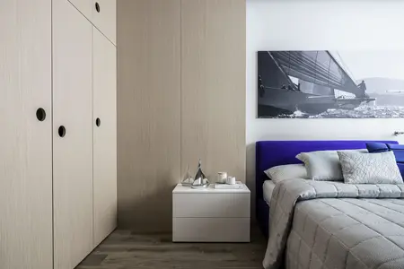 Wnętrze sypialni w stylu skandynawskim z szarym łóżkiem i białymi meblami.