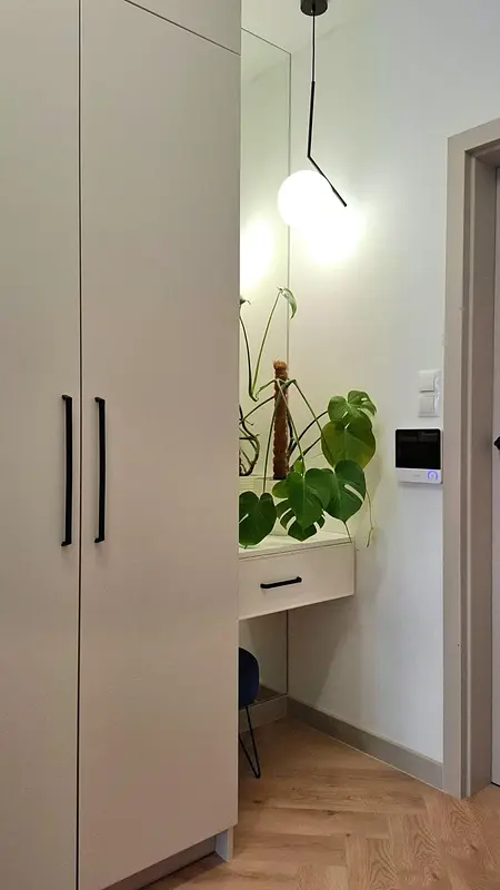 Garderoba z białymi meblami, lustrem i zieloną rośliną