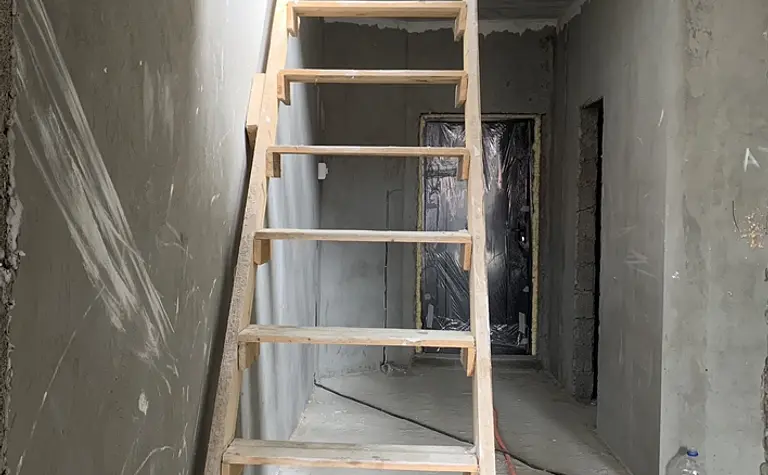 Korytarz z drewnianymi schodami i szarymi ścianami w stylu eklektycznym.