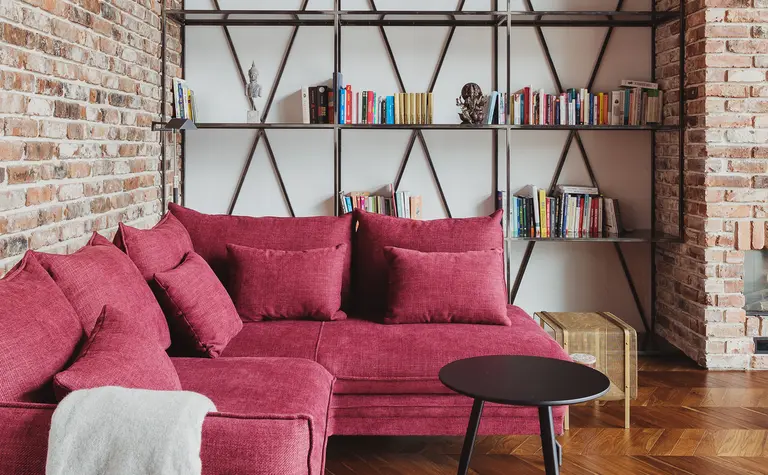 Wnętrze salonu w stylu dopamine decor z czerwoną sofą, ceglaną ścianą i drewnianą podłogą.