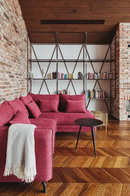 Wnętrze salonu w stylu dopamine decor z czerwoną sofą, ceglaną ścianą i drewnianą podłogą.