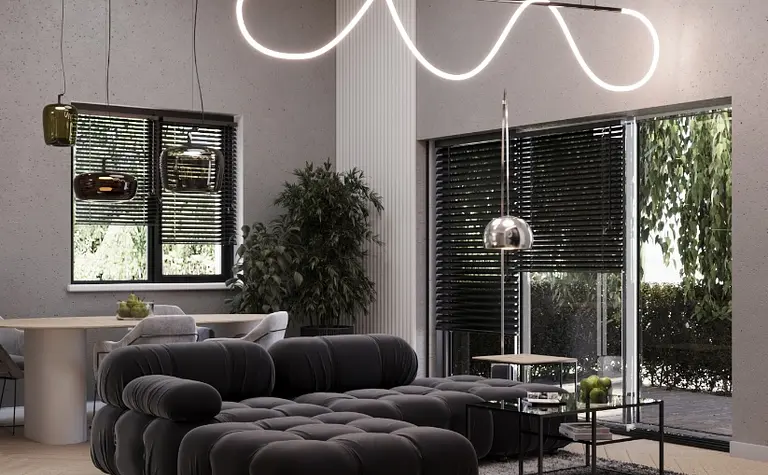 Przestronny salon z czarną, pikowaną sofą, oryginalnym oświetleniem LED w formie fali i dużymi oknami. Elegancki stolik kawowy i rośliny dodają wnętrzu stylu i świeżości.