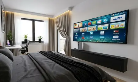 Sypialnia z telewizorem Smart TV na ścianie, szarą pościelą i biurkiem, styl współczesny, nowoczesny i tradycyjny