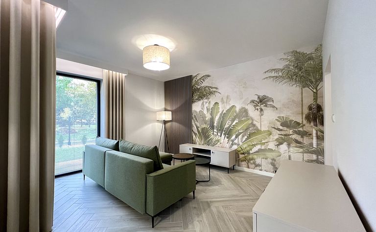 Wnętrze salonu w stylu boho i współczesnym z zieloną sofą i palmową tapetą.