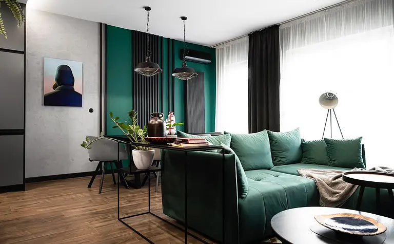 Wnętrze salonu z zieloną sofą, industrialnymi lampami i roślinnymi dekoracjami.