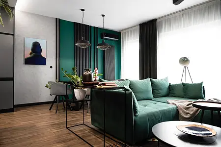 Wnętrze salonu z zieloną sofą, industrialnymi lampami i roślinnymi dekoracjami.